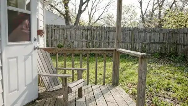 A man in his sixties stepping onto his back porch with a glass of water and sitting down to look at the yard